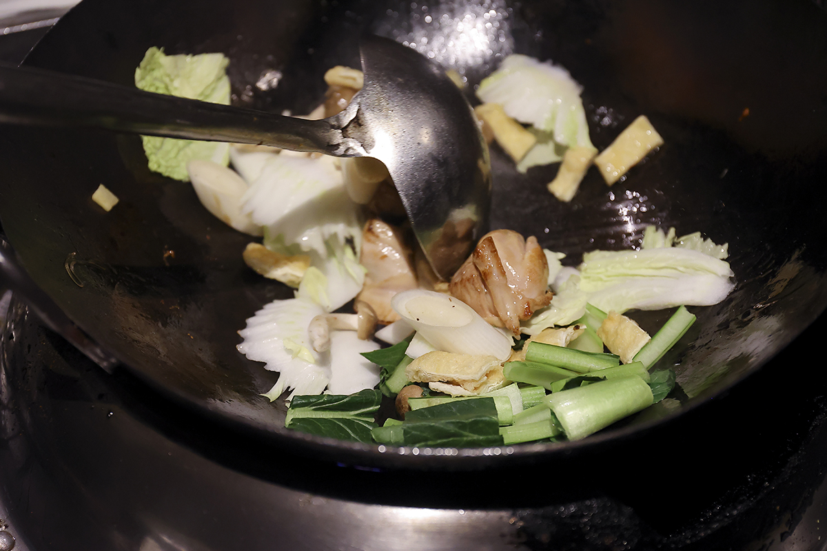 ②<br />
フライパンにサラダ油を入れ、中火にかけてよく熱したところに鶏もも肉、白ネギとショウガ入れ、表面がカリッと香ばしくなるまで炒める。白菜、小松菜、しめじ、筍、うすあげを加えて炒める。水と鶏ガラスープを加えて煮る。